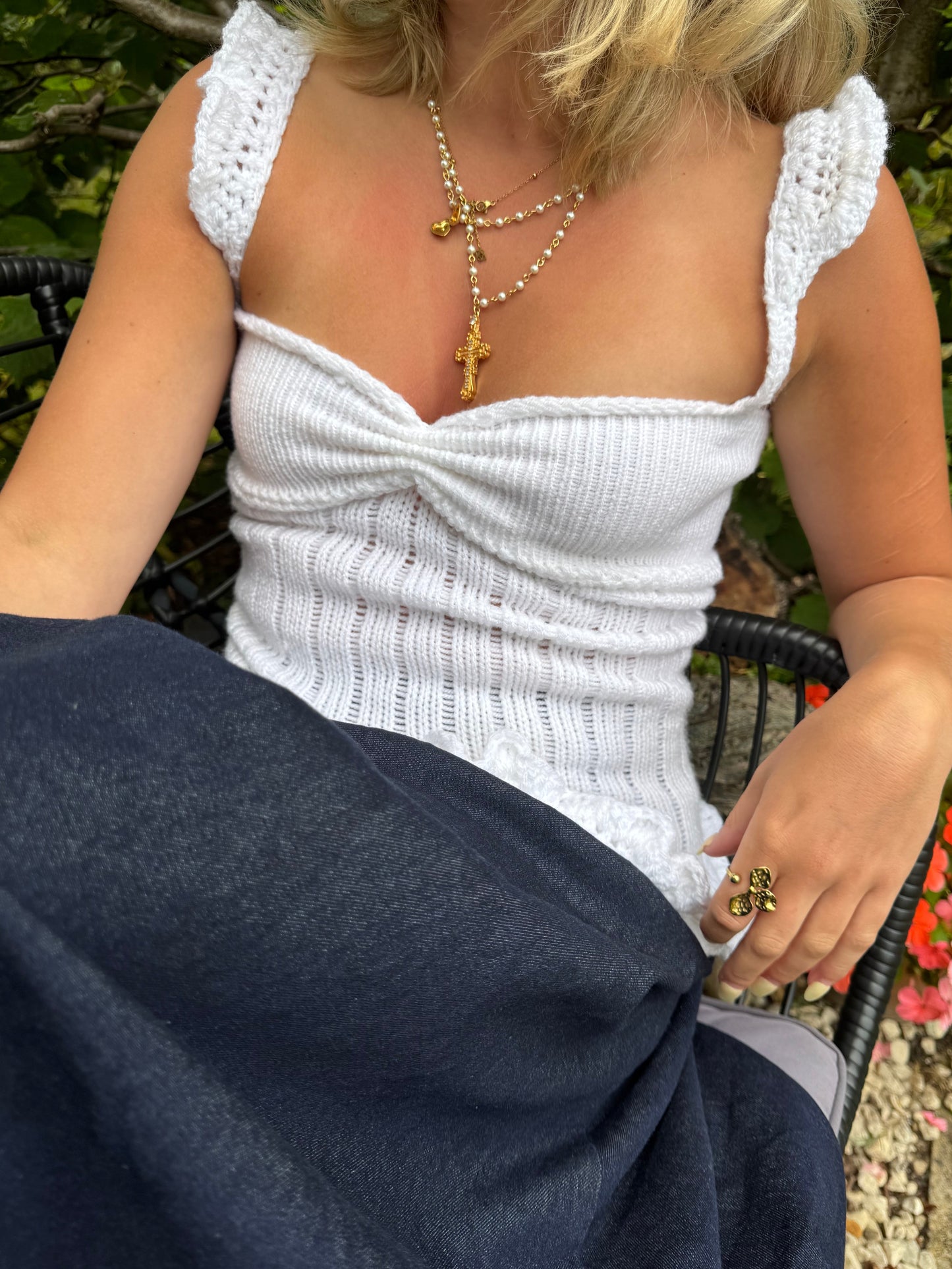 Person wearing a white crochet top with ruffled edges, sitting outdoors.