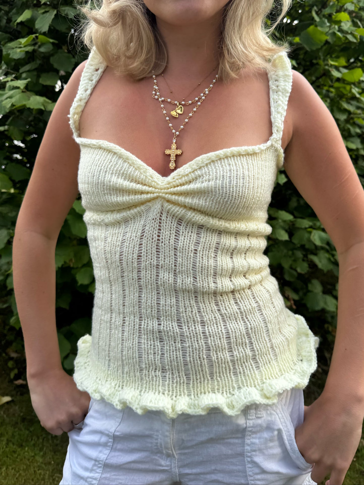 Woman wearing a light-colored knitted top with a green leafy background