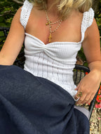 Person wearing a white crochet top with ruffled edges, sitting outdoors.
