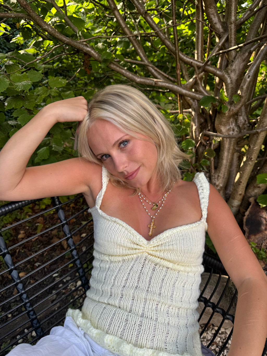 Woman in a light-colored  yellow knit top sitting outdoors with greenery in the background